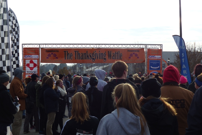 Runners mingling in front of an orange banner reading "The Thanksgiving Wattle"